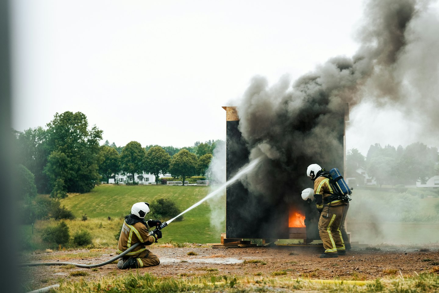 Due vigili del fuoco si esercitano a spegnere una struttura in legno in fiamme all'aperto.